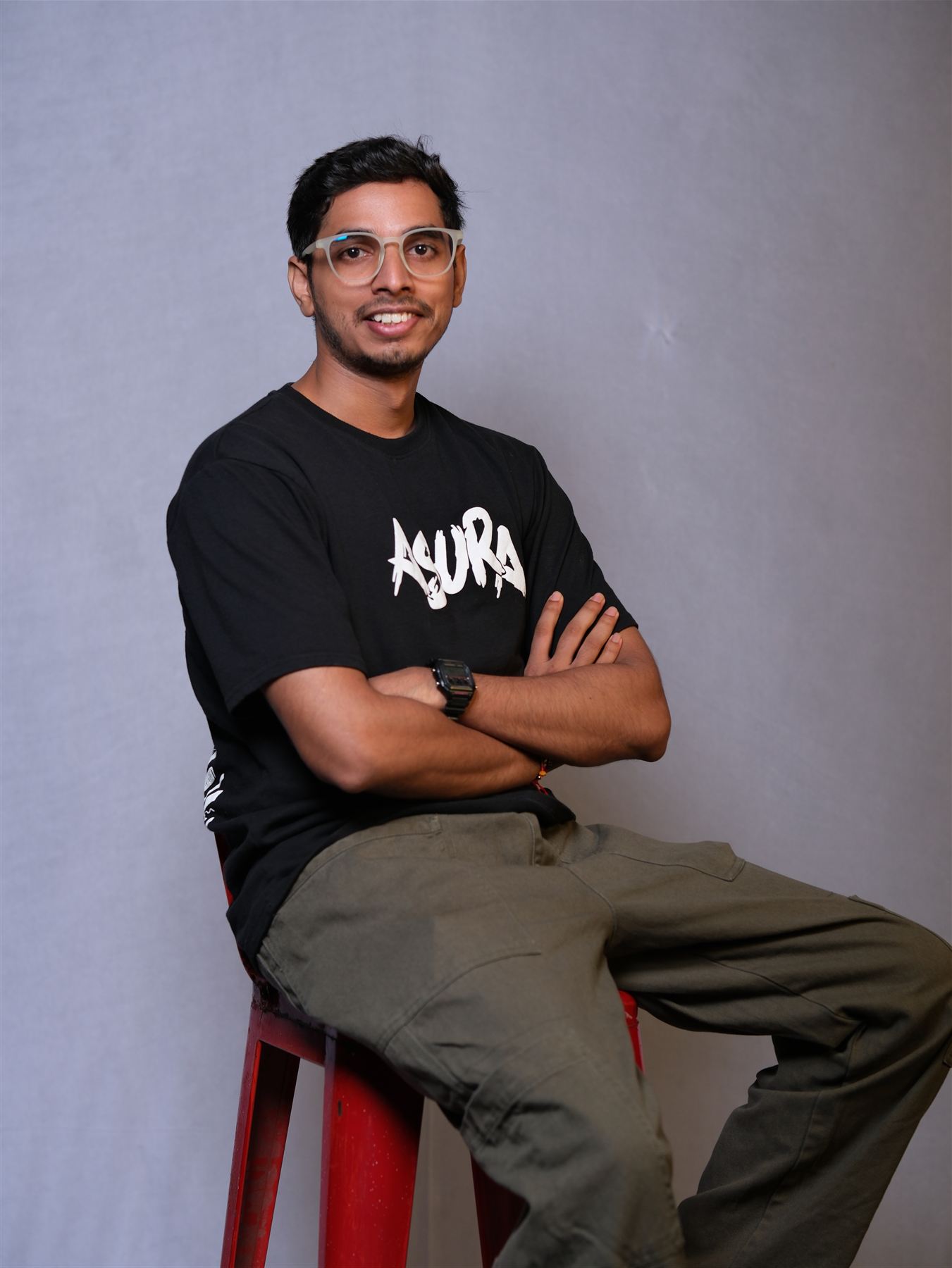 Portrait of Pradyumn sitting on a red stool, arms crossed, smiling